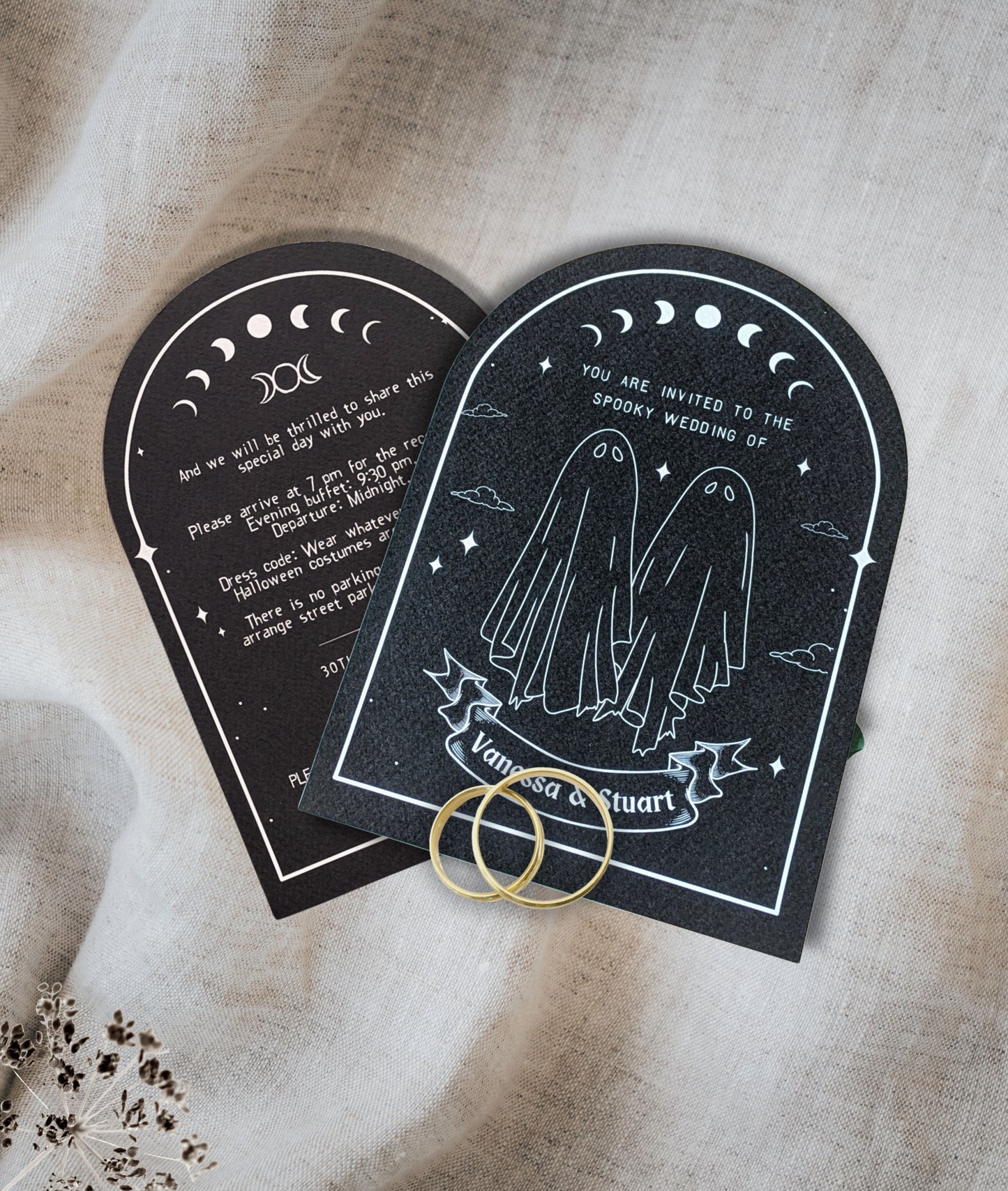 Black invitation cards with ghost couple and moon phase design, white text and design on a beige fabric background