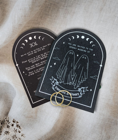 Black invitation cards with ghost couple and moon phase design, white text and design on a beige fabric background